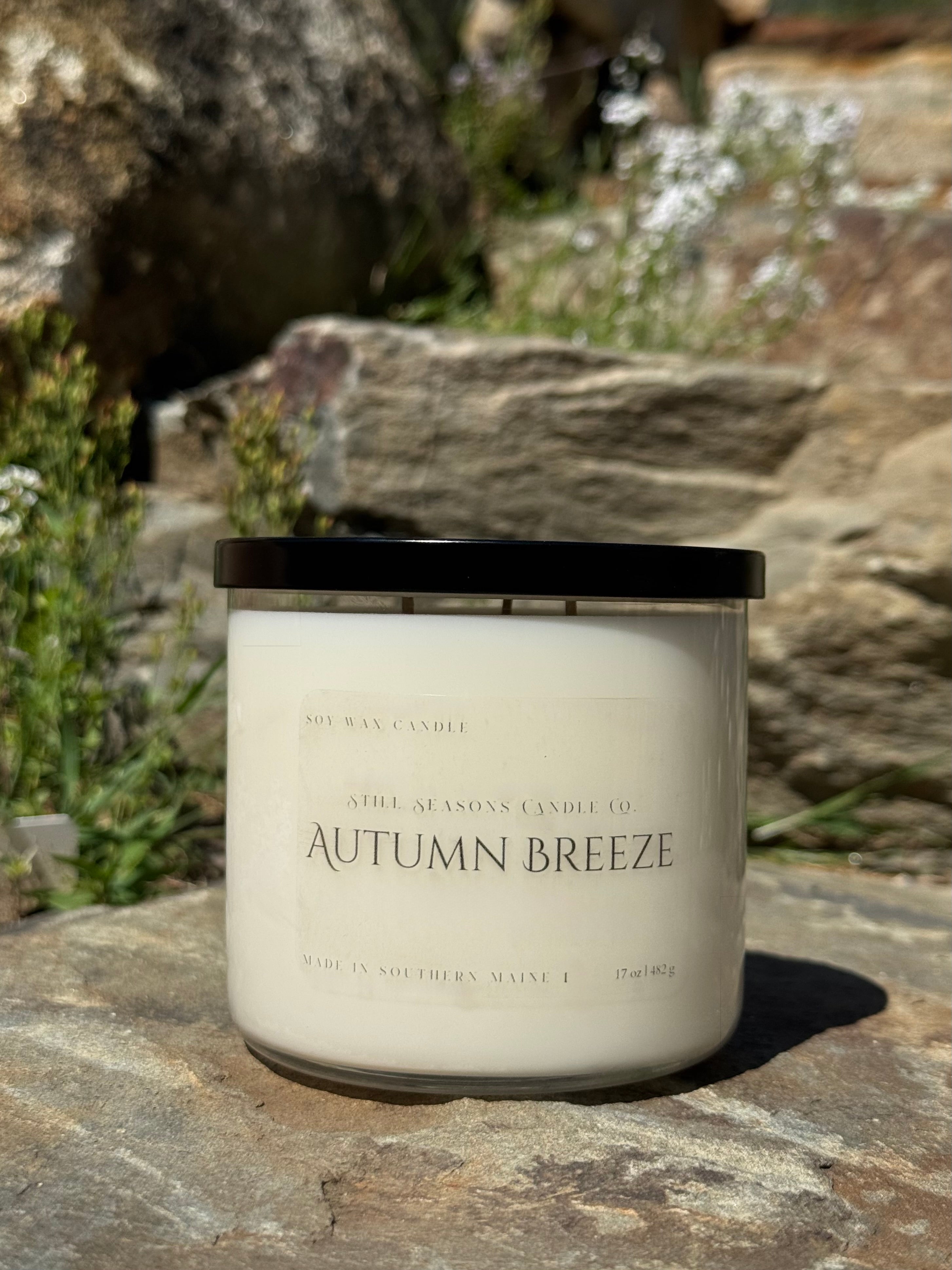 Candle labeled 'Autumn Breeze' on a stone surface with natural background