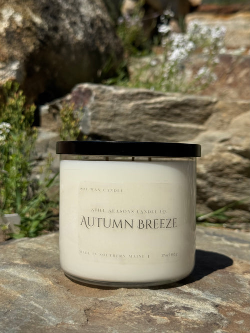 Candle labeled 'Autumn Breeze' on a stone surface with natural background