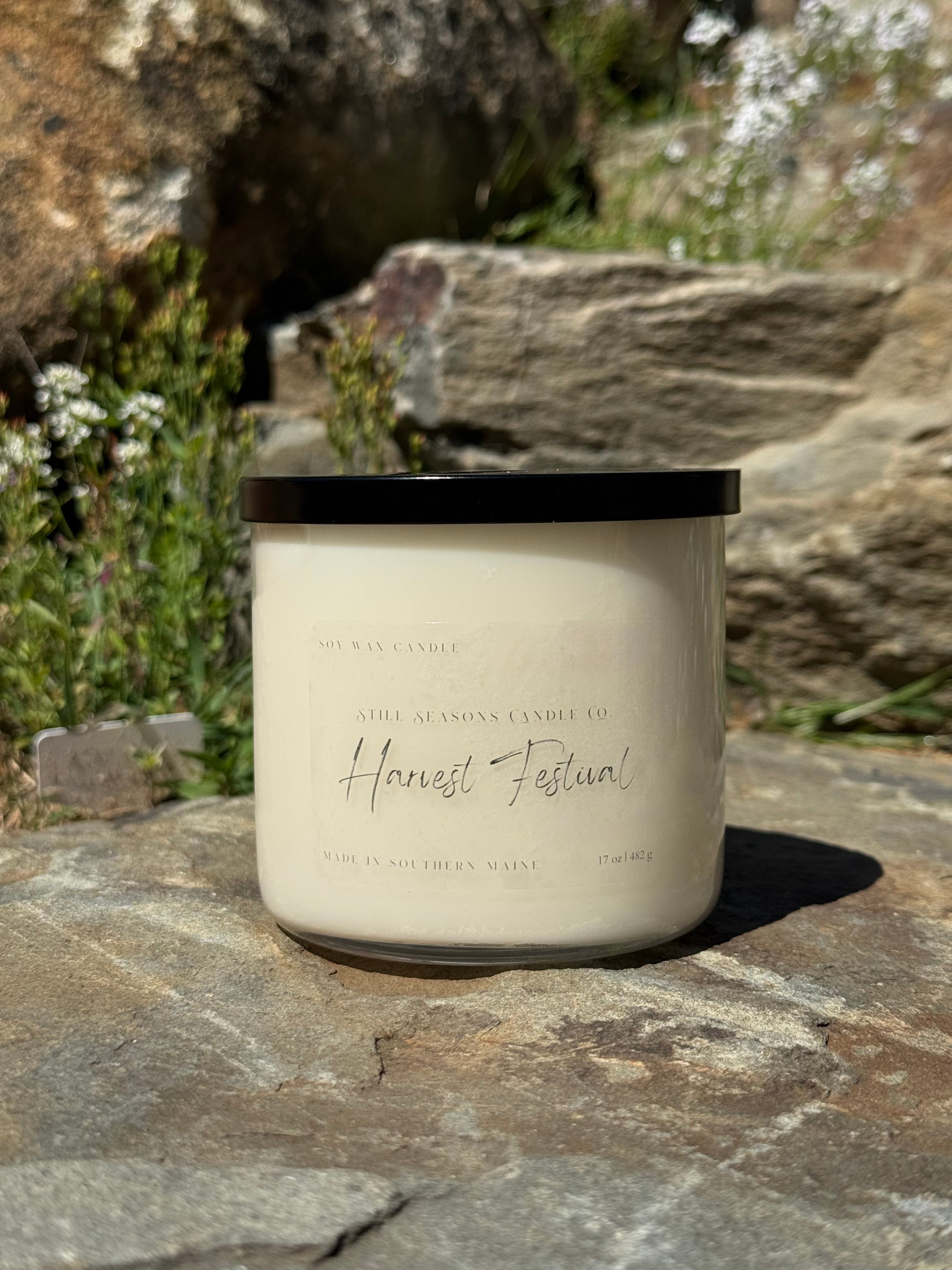 Candle labeled 'Harvest Festival' on a stone surface with natural background