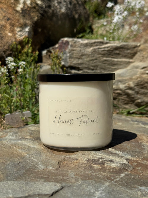 Candle labeled 'Harvest Festival' on a stone surface with natural background