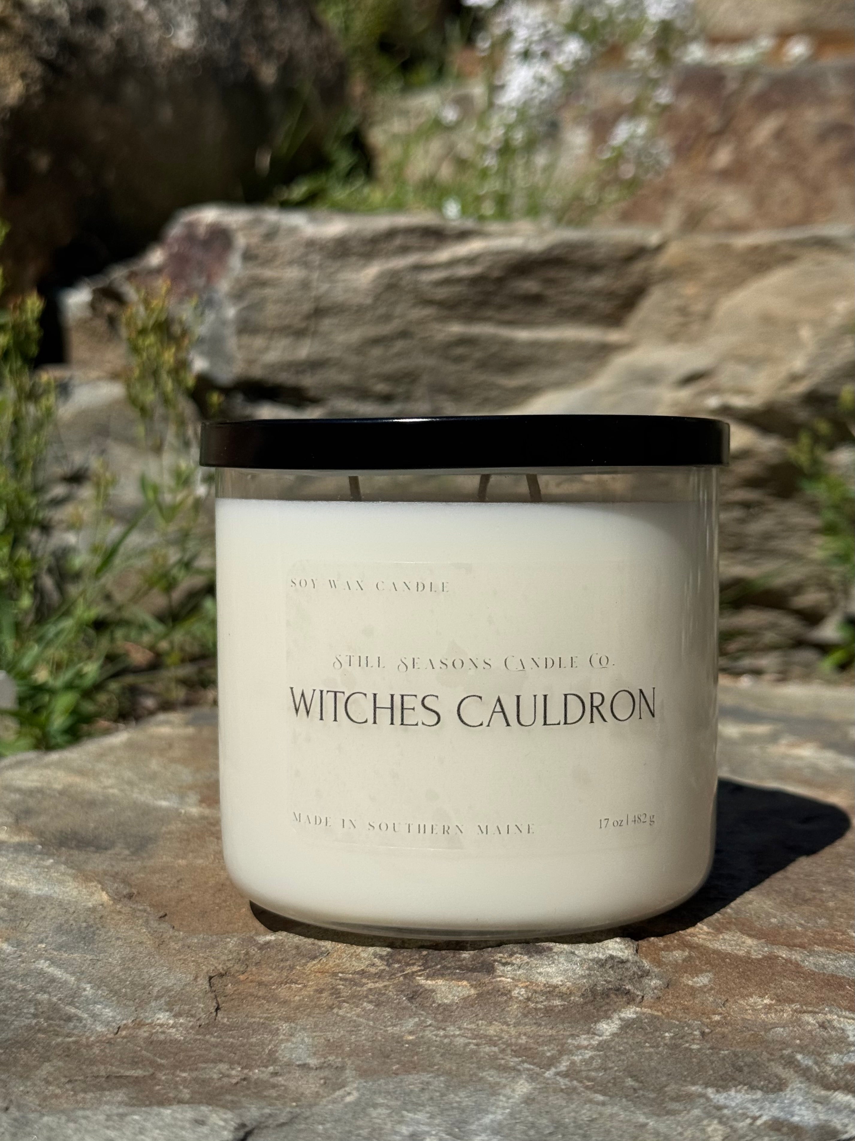 Candle labeled 'Witches Cauldron' on a stone surface with natural background